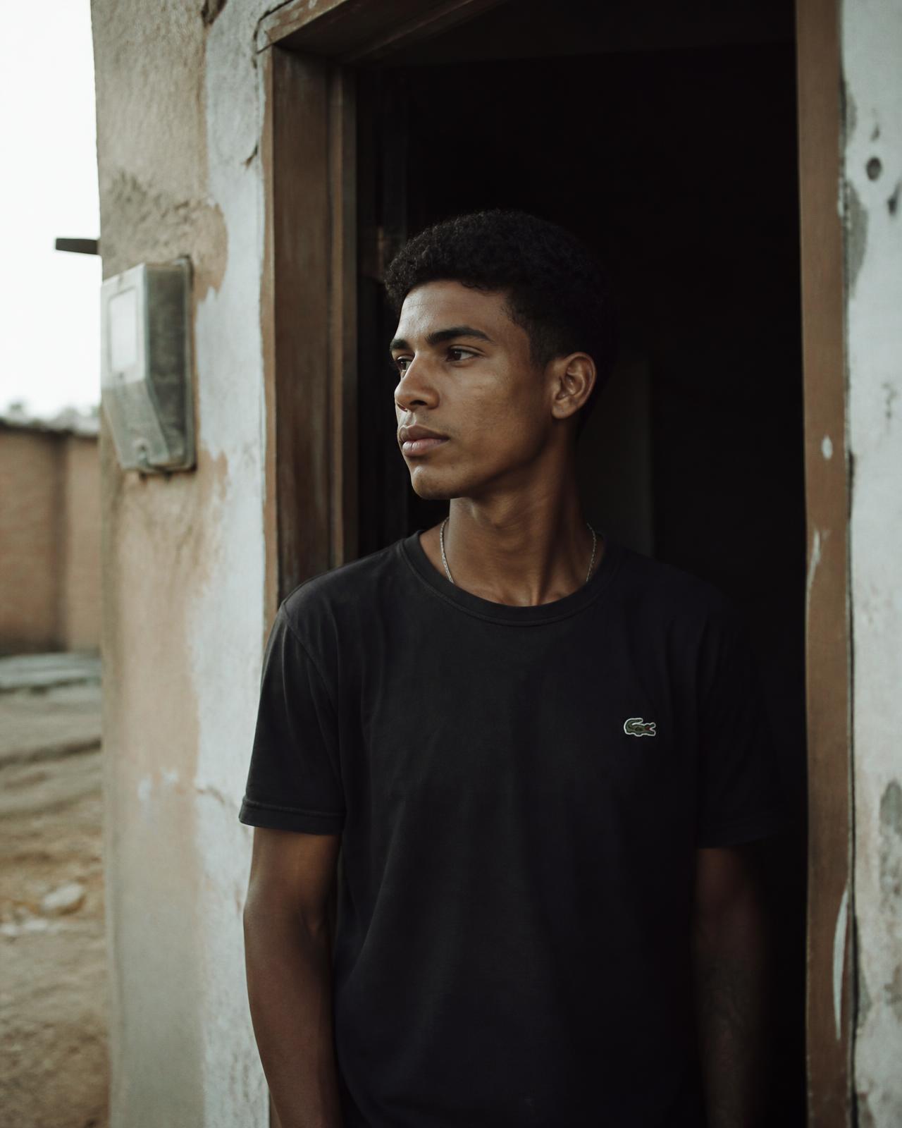 Jovem brasileiro na porta de casa, em um fim de tarde, olhando para a rua